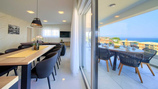 Un espace de restauration moderne, doté d’une longue table, de chaises et offrant une vue sur la mer grâce à de grandes fenêtres.
