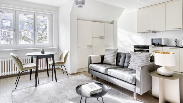 Een moderne woonkamer met een grijze bank, een ronde salontafel en een eethoek met stoelen.