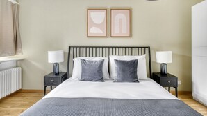 Een slaapkamer met een bed, twee nachtkastjes met lampen, een radiator en twee ingelijste foto's aan de muur.
