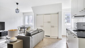 Een moderne keuken met witte kastjes, een eethoek met tafel en stoelen, een bank en een televisie.