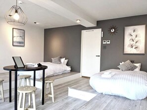 A modern bedroom with two beds, a desk with stools, a large window, and a decorative wall piece.