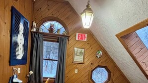 Un interior de madera con una mesa de comedor, sillas, un banco, una escalera y vistas a árboles por una ventana.