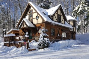 Una baita di legno con tetto imbiancato dalla neve, immersa in un paesaggio innevato e alberato.