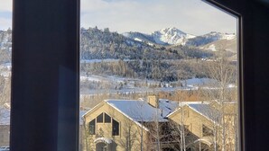 Vista desde una ventana de un edificio sobre un paisaje nevado, incluyendo montañas y árboles.