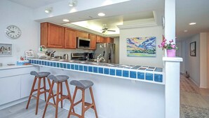 A kitchen with wooden cabinets, a tiled backsplash, a refrigerator, and a clock on the wall.