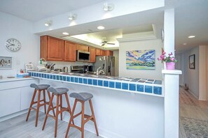 A kitchen with wooden cabinets, a tiled backsplash, a refrigerator, and a clock on the wall. - Snug Harbor 124 Gulf Front three bedroom exclusive vacation rental (Sanibel)