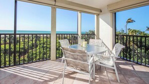 A balcony with a table and chairs, a ceiling fan, and a view of the ocean.