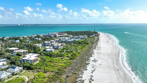 An aerial view of a coastal resort with beachfront properties, a marina, and a bridge in the background.