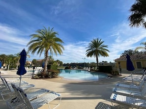 Ein Poolbereich mit Liegestühlen und Sonnenschirmen, Palmen und blauem Himmel.
