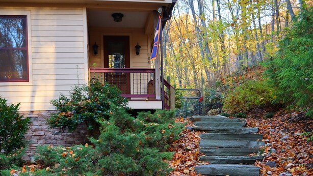 Eine Steintreppe führt zu einem Haus mit einer Veranda, umgeben von Herbstlaub und Bäumen.