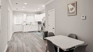 Een moderne keuken met witte kasten, een eettafel met stoelen en een lijst met een afbeelding aan de muur.