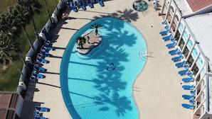 Ein Luftbild eines Schwimmbeckens mit Liegestühlen und einer kleinen Insel, umgeben von einem Gebäude mit mehreren Balkonen.