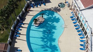 An aerial view of a swimming pool with lounge chairs and a small island, surrounded by buildings.
