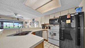 A modern kitchen with a black refrigerator, stainless steel appliances, and a window with a view.