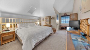 A bedroom with a large bed, a television, a desk, and a window.