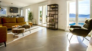 A spacious living area with a yellow sofa, a wooden coffee table, and a leather armchair. There is a bookshelf and a view of the outdoors through large windows. - Villa Cara Mull Alcalalí by Interhome (Dénia)
