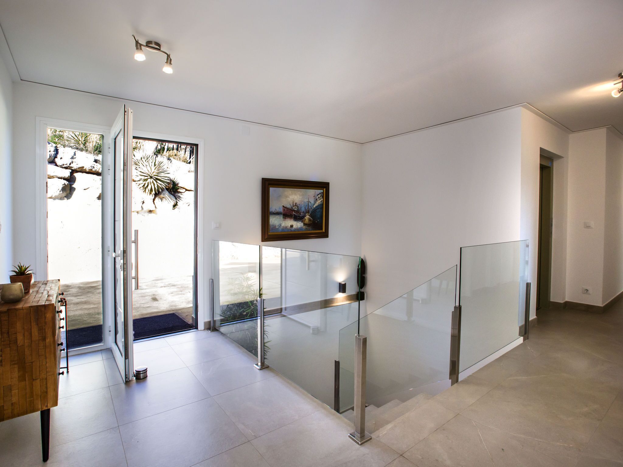 A modern interior with a glass staircase, a wooden bench, and a framed painting on the wall.