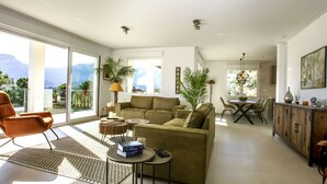 A spacious living room with a sofa, a coffee table, and a dining area with a table and chairs. There are large windows offering a view of the outdoors. - Villa Cara Mull Alcalalí by Interhome (Dénia)