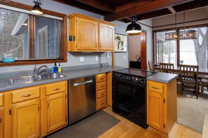 A kitchen with wooden cabinets, a stainless steel dishwasher, and a black stove.
