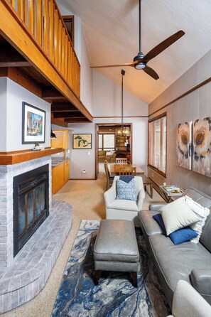A spacious living area with a fireplace, a sofa, a dining table, and a ceiling fan.