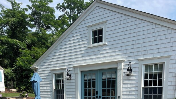 A white house with a blue door and windows, a brick patio, and outdoor furniture. - The Rose Cottage of Sandwich Village (Sandwich)