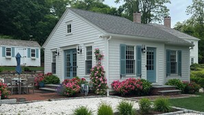 A white house with blue shutters, a brick porch, and a garden with pink flowers. - The Rose Cottage of Sandwich Village (Sandwich)