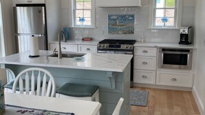 A modern kitchen with white cabinetry, a stainless steel refrigerator, a gas stove, and a coffee maker. - The Rose Cottage of Sandwich Village (Sandwich)
