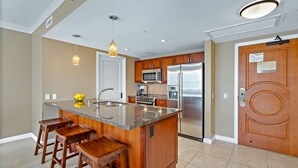 A modern kitchen with a central island, wooden bar stools, stainless steel appliances, and pendant lighting.