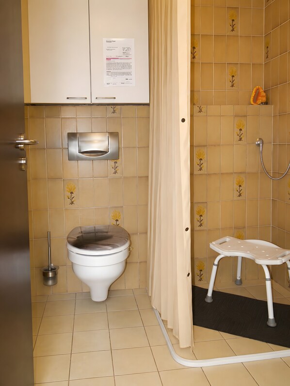 Une salle de bain équipée de toilettes, d’un sèche-mains, d’un rideau de douche et d’un petit marchepied.