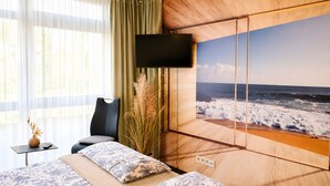 A bedroom with a bed, a TV, a window with curtains, and a wall mural of the ocean.