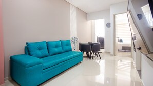 A modern living room with a teal sofa, a dining table with chairs, and a staircase leading to another level. - Montepinares Apartaestudios (Montería)