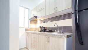 A modern kitchen with light wood cabinets, a black refrigerator, and a tiled backsplash. - Montepinares Apartaestudios (Montería)