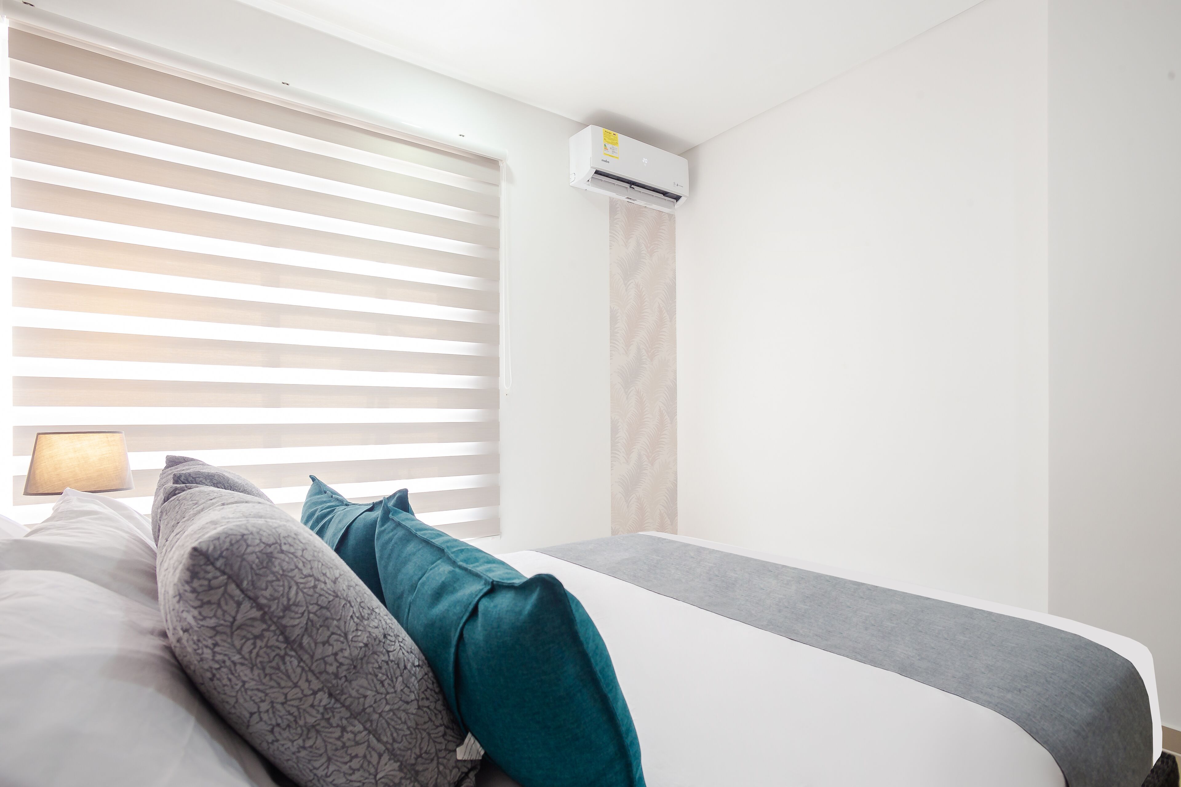 A modern bedroom with a bed, a nightstand, a lamp, and a wall-mounted air conditioner.