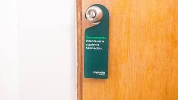 Una puerta de madera con una etiqueta verde que dice "Descanse. Intenta en la siguiente habitación." y el logo "ayenda hotels".