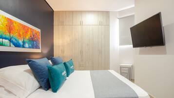 A modern bedroom with a bed, teal pillows, a colorful painting, a TV, and a laundry service sign.