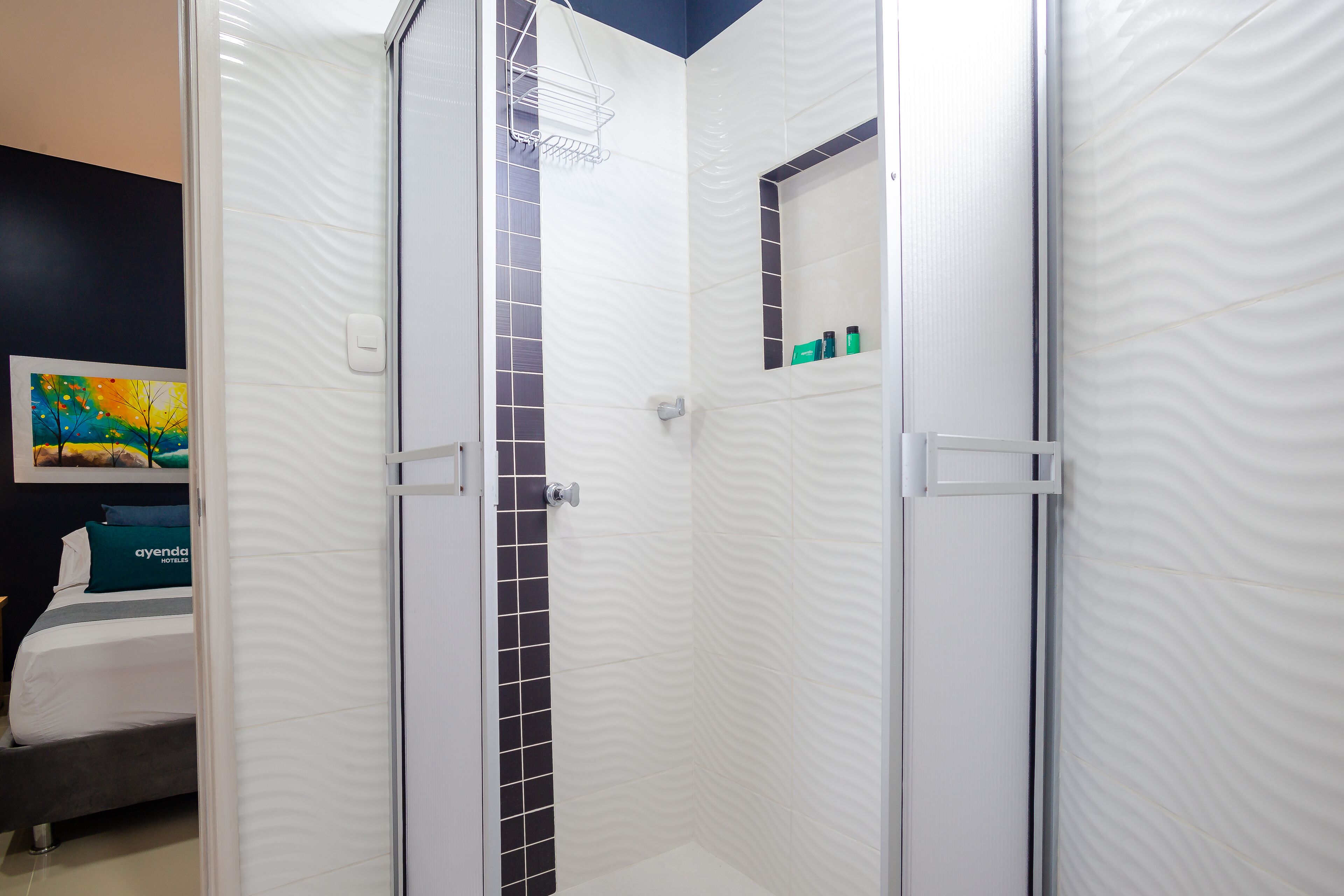 Un baño moderno con ducha, un estante pequeño con artículos de aseo y un cuadro en la pared.