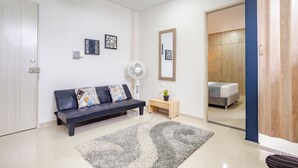A modern living room with a dark leather sofa, a small wooden side table, a floor lamp, and a large mirror on the wall. - Montepinares Apartaestudios (Montería)