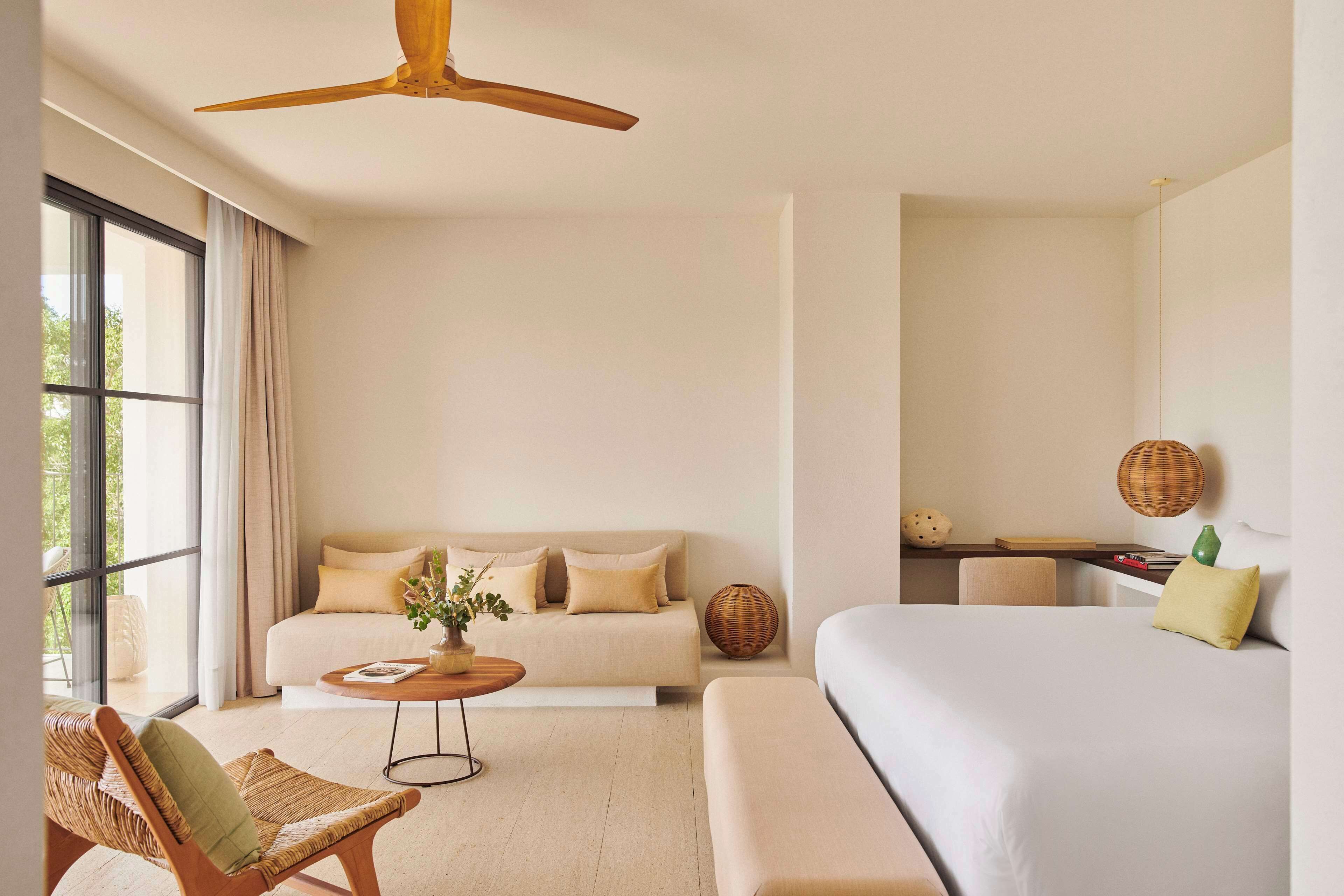 A modern hotel room with a large bed, a sofa, a dining table, and a ceiling fan.