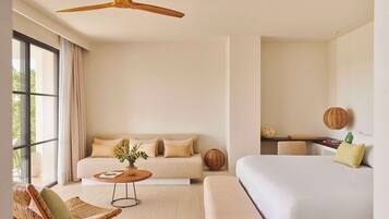 A modern hotel room with a large bed, a sofa, a dining table, and a ceiling fan.