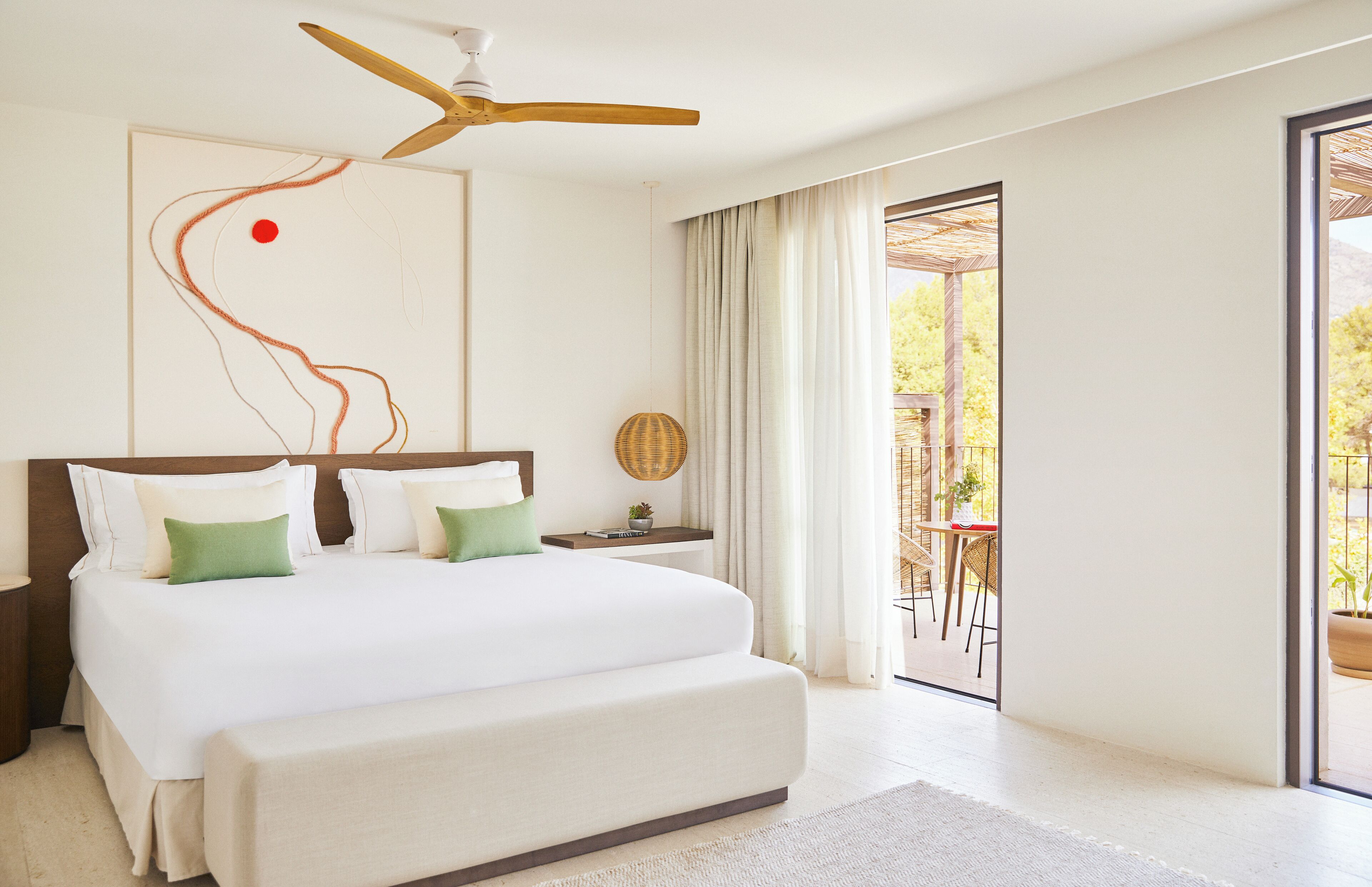 A modern hotel room with a large bed, a ceiling fan, a view of the outdoor patio, and a large abstract painting on the wall.