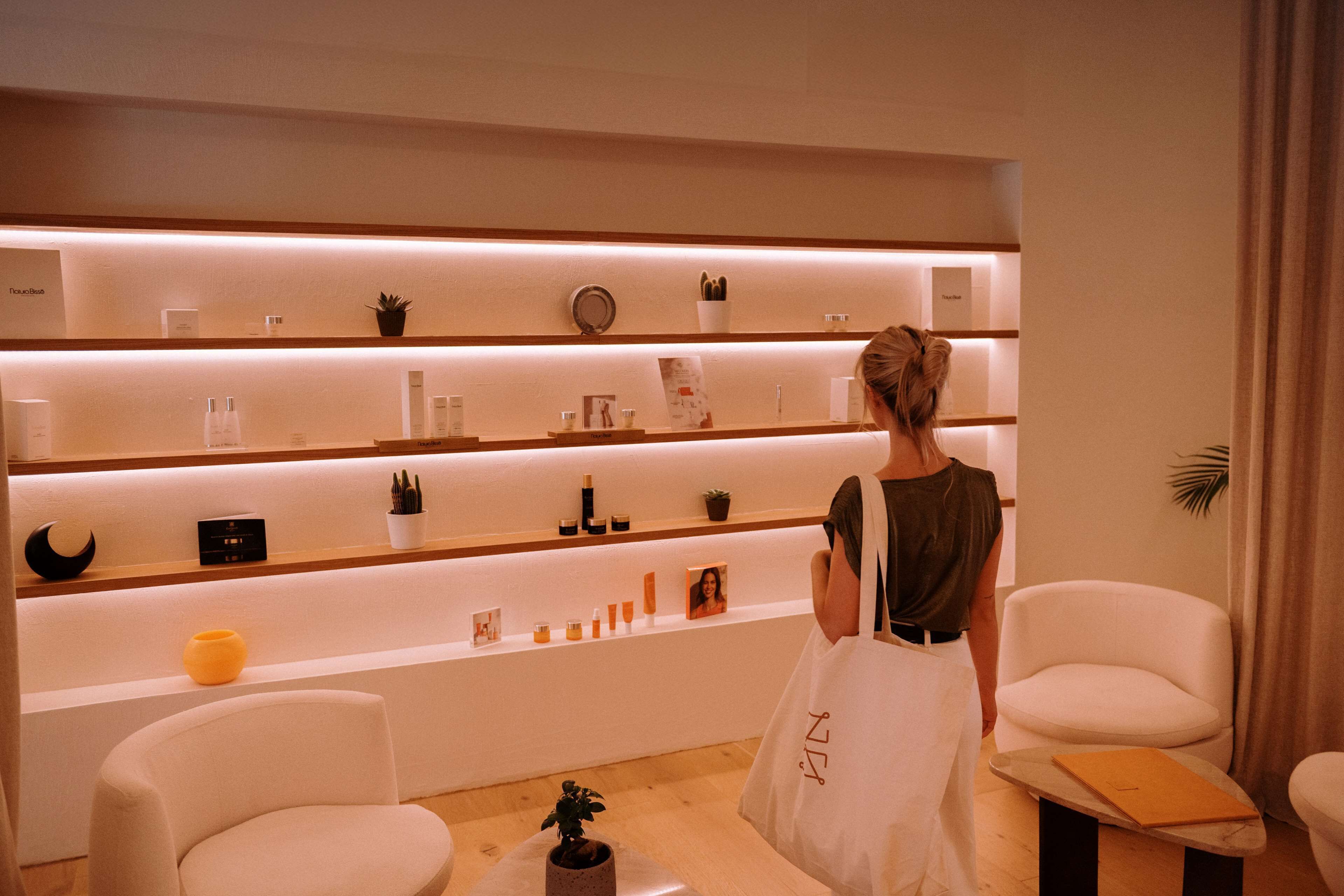 Un interior moderno con un mostrador de recepción, sillas blancas y estanterías con distintos objetos.