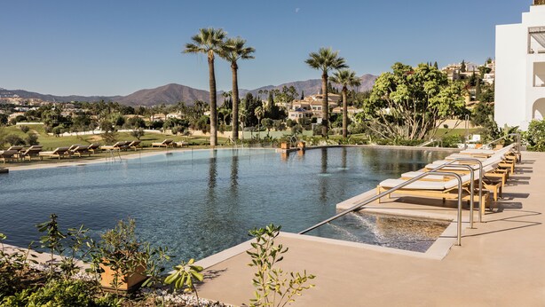 Una piscina con sillas de descanso, palmeras y vistas a las montañas.