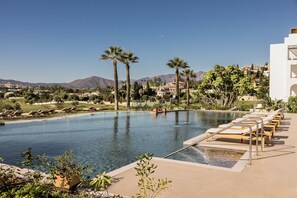 Una piscina con sillas de descanso, palmeras y vistas a las montañas.