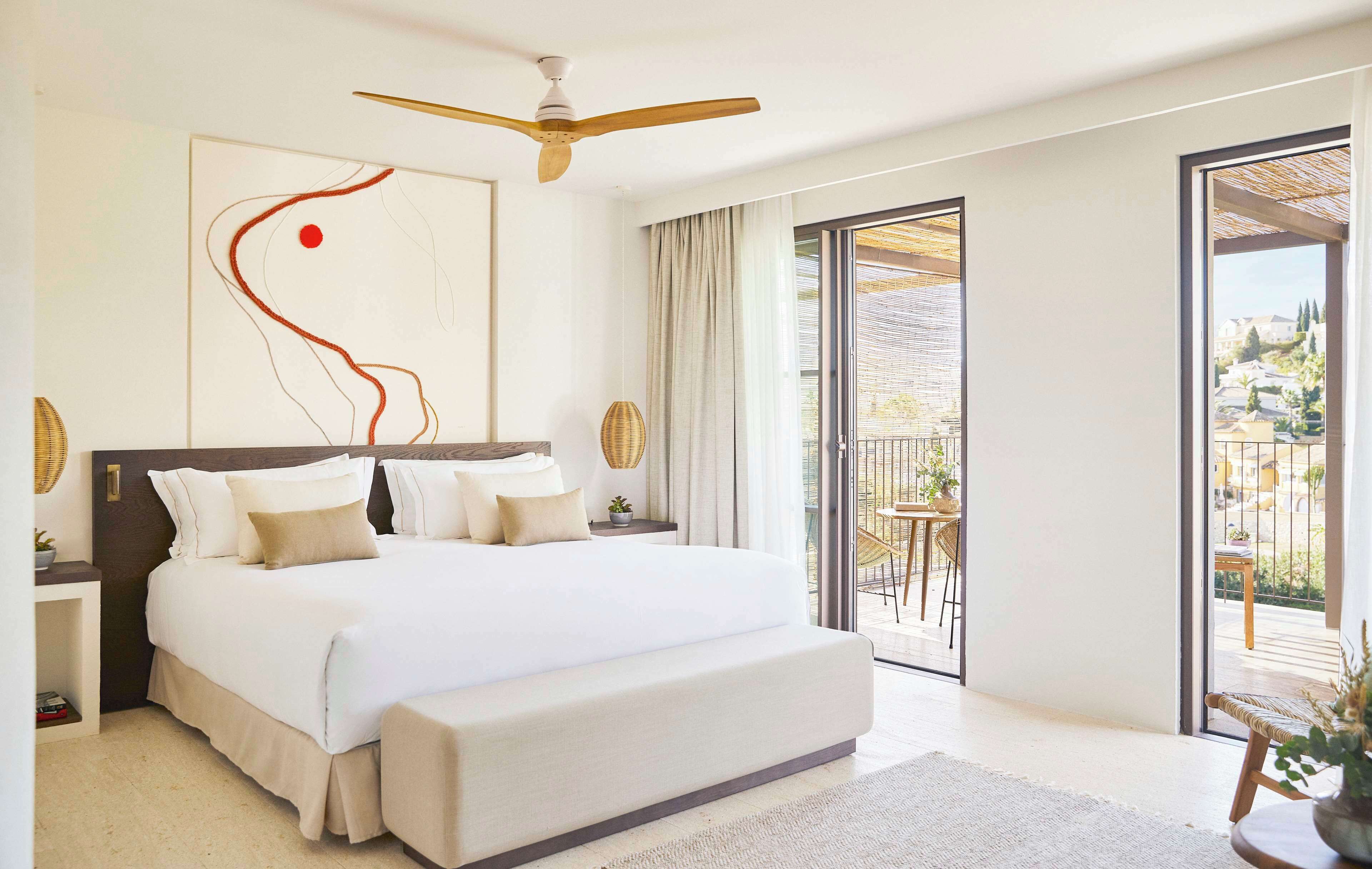 Un dormitorio moderno con una cama grande, un ventilador de techo y vistas a un balcón con mobiliario exterior.