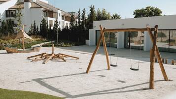 A modern outdoor area with a swing set, a wooden bench, and a small table.