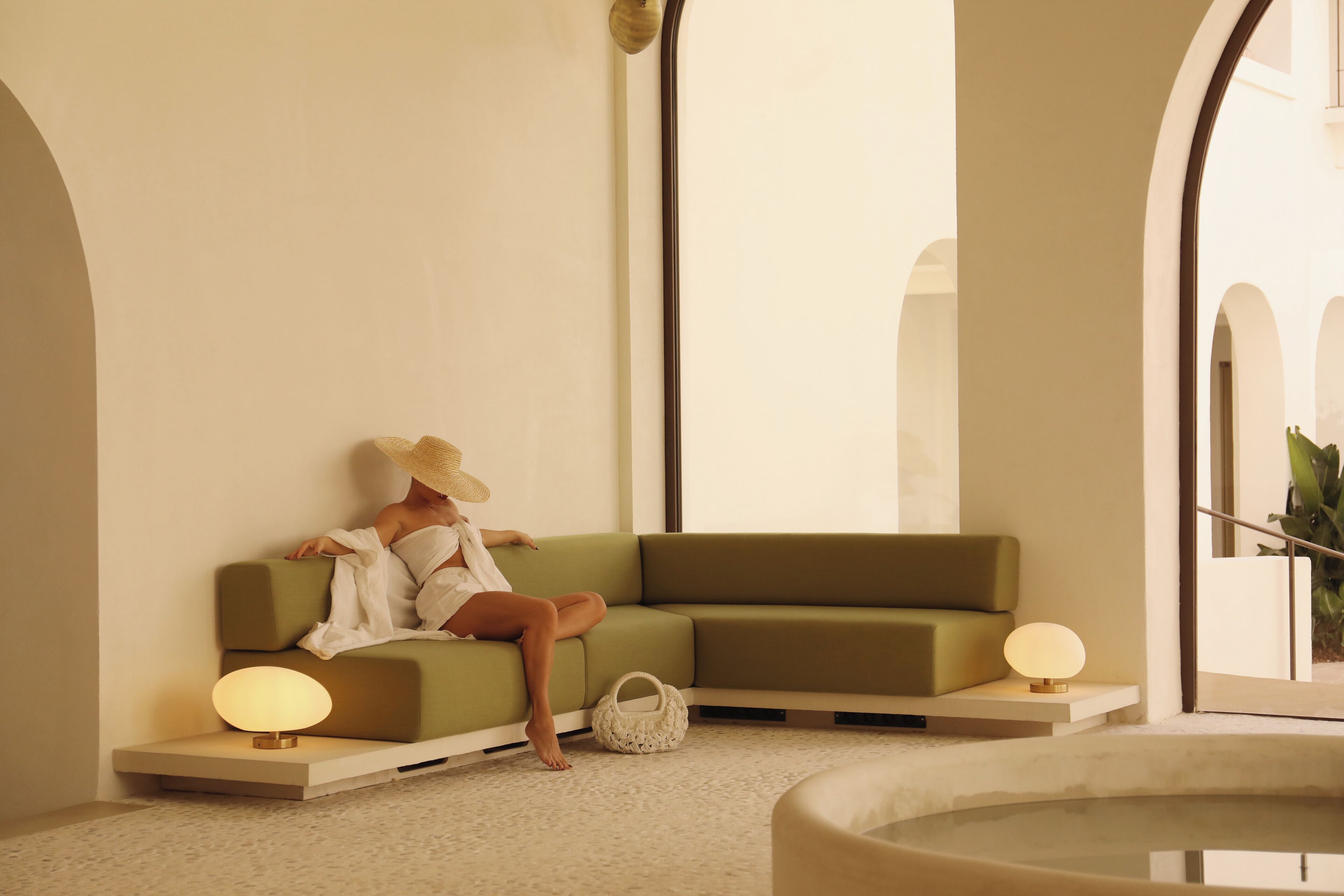 Een modern interieur met een groene bank, een klein tafeltje met een lamp en een decoratieve schaal.