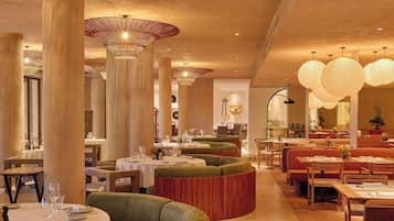 Un restaurante con mesas redondas, asientos acolchados verdes y farolillos de papel colgantes.