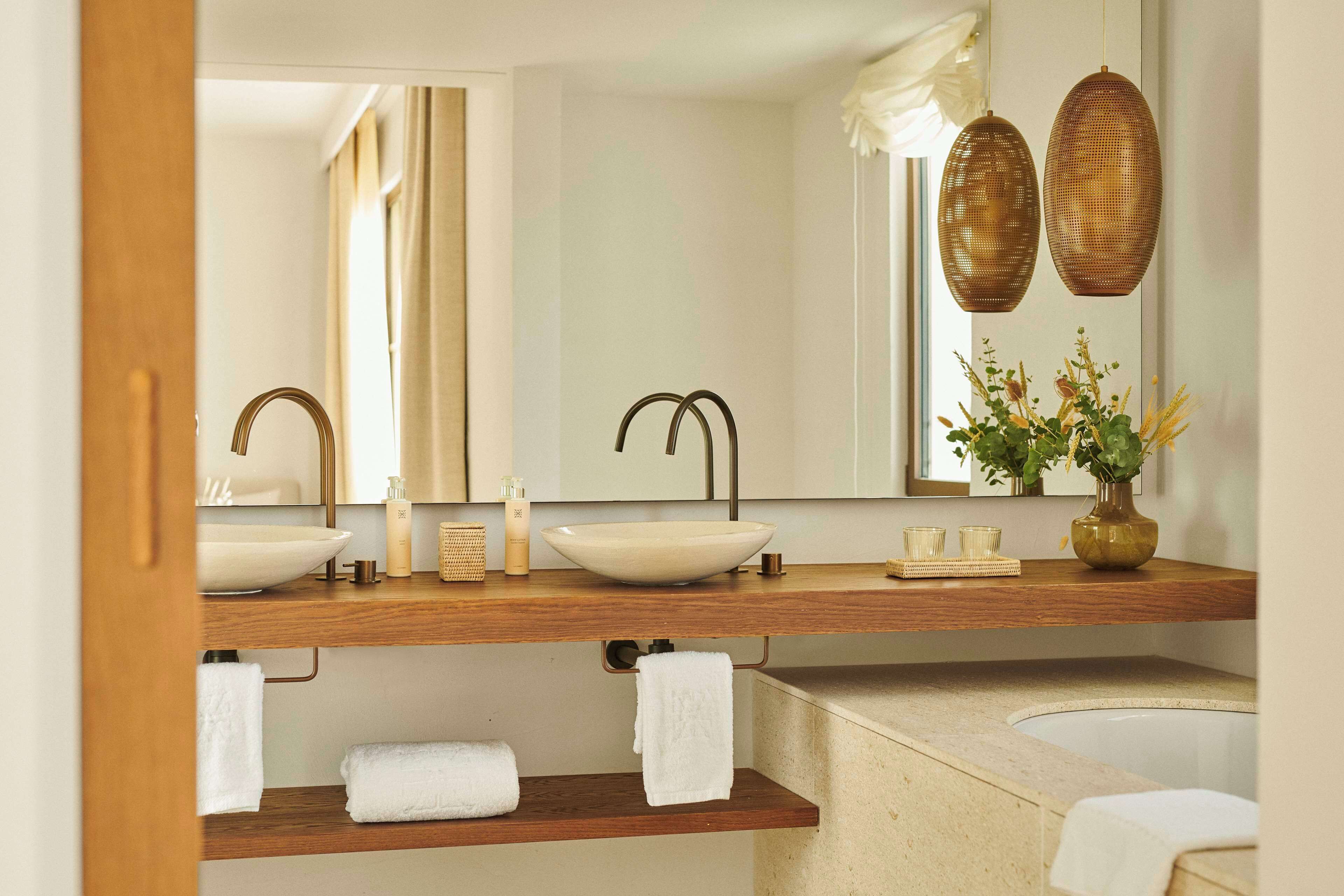 Une salle de bain avec deux lavabos, un grand miroir et un vase rempli de fleurs.