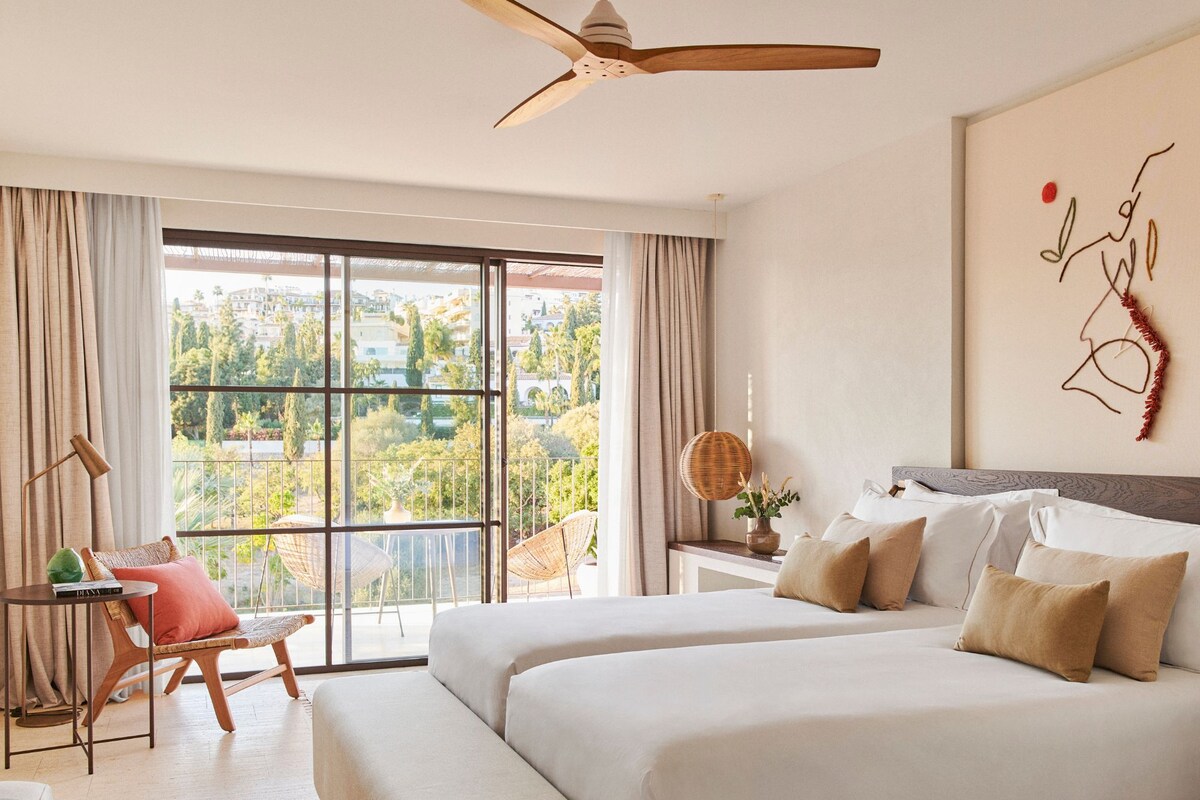 Un dormitorio con una cama grande, un escritorio, una silla y vistas al exterior.
