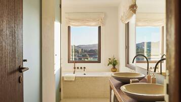 A bathroom with a bathtub, two sinks, and a window with a view of a landscape.